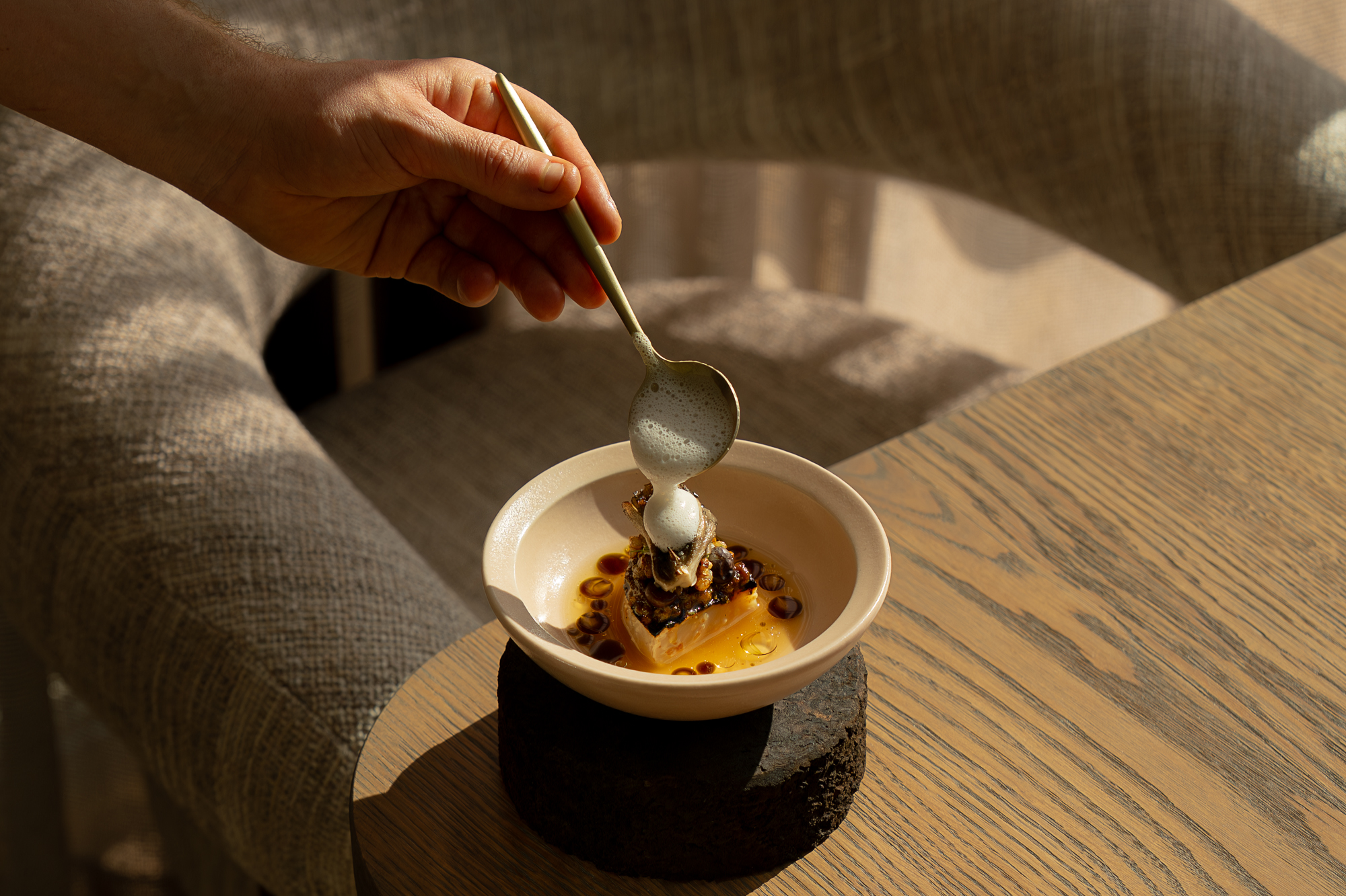 Conscious fine dining dish at Restaurant Flore with a chef delicately placing a spoonful of foam on top as a finishing touch.