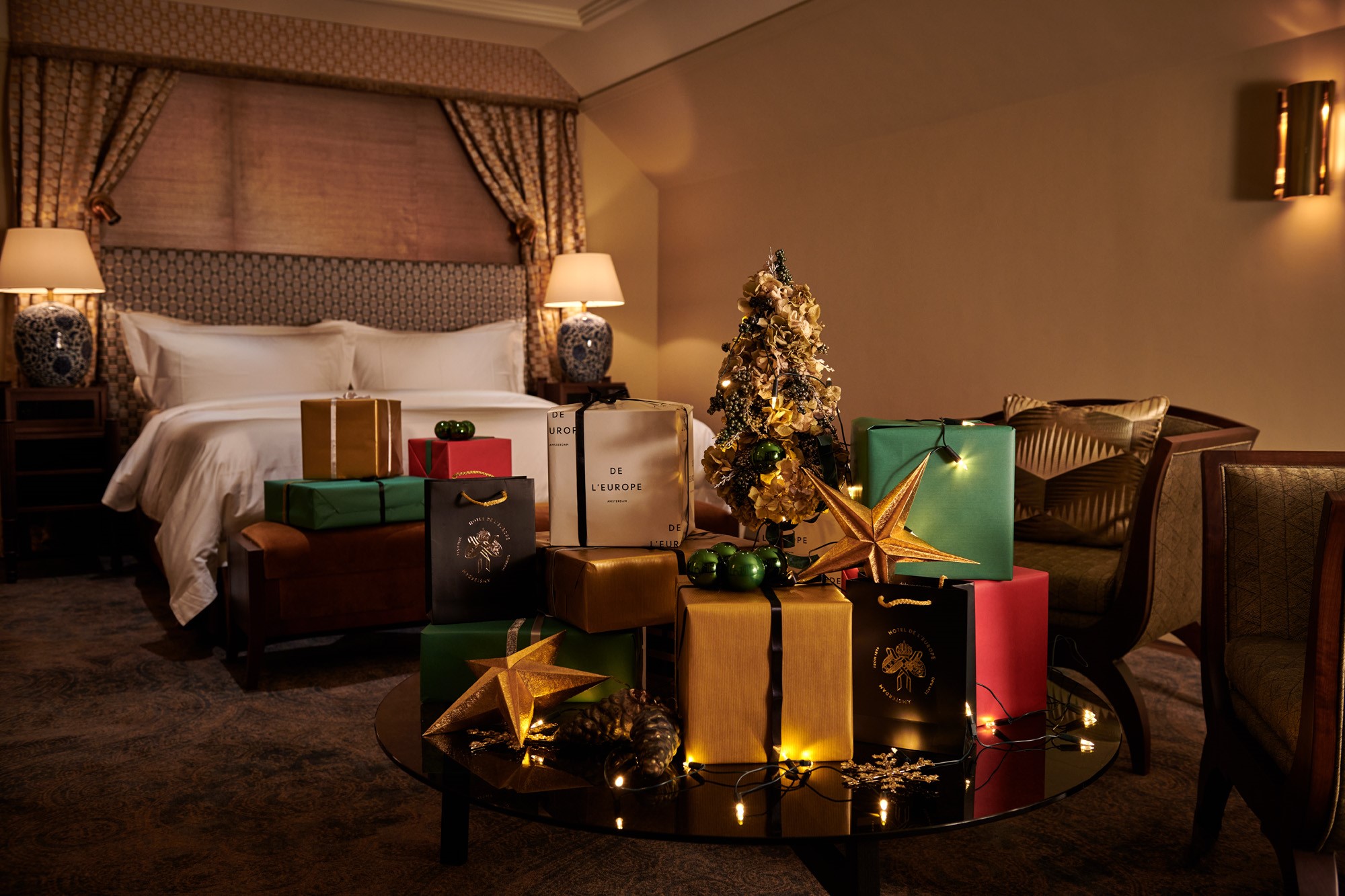 Festliche Szene mit einem Hotelbett im Hintergrund und einer Fülle von Weihnachtsgeschenkpaketen, die davor aufgestapelt sind und eine fröhliche Weihnachtsstimmung verbreiten.