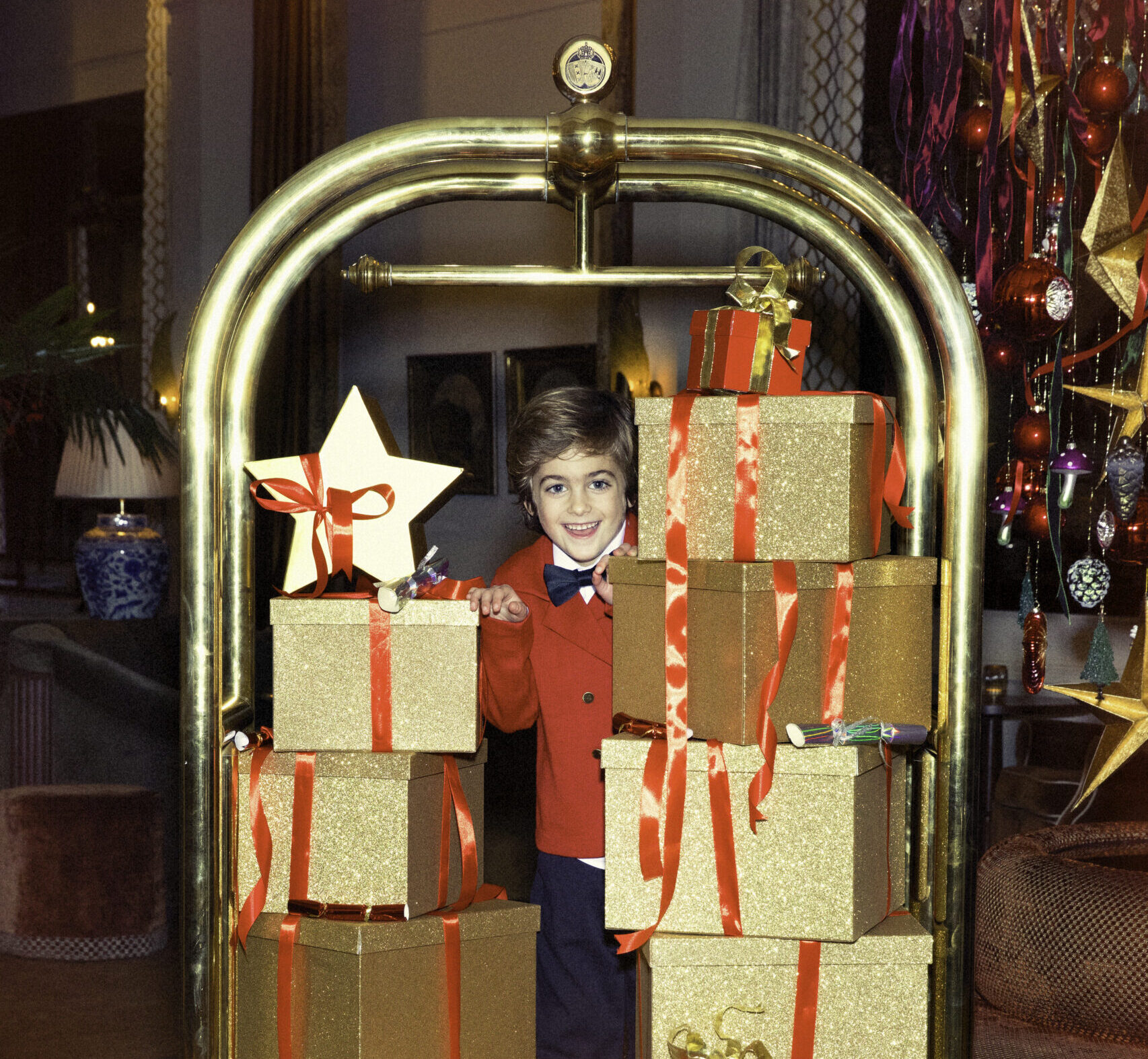 Playful child hiding behind a luggage cart filled with festive presents